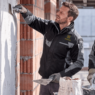 Ein Mann verputzt eine Wand und trägt eine individuell besticke Premium-Arbeitsjacke