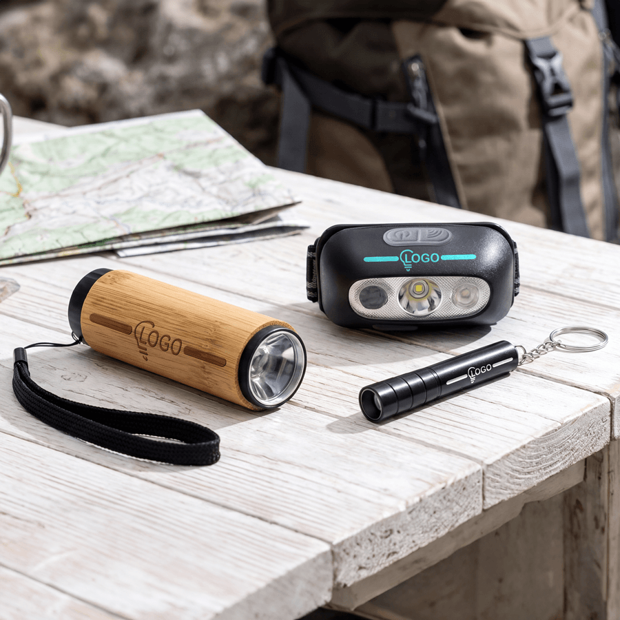 Unterschiedliche Werbetaschenlampen personalisiert mit Ihrem Logo auf einem Outdoortisch